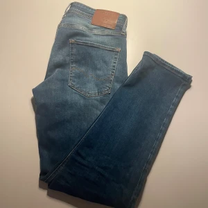 Blå tapered jeans från Jack & Jones - Snygga blå jeans från Jack & Jones i modellen Tapered/Mike. Jeansen har klassisk femficksdesign, ljus tvätt och bruna sömmar. Tillverkade i mjukt denimtyg med en bekväm passform som smalnar av nedtill. Perfekta för en avslappnad stil. Skick 10/10 ‼️FAST PRIS‼️