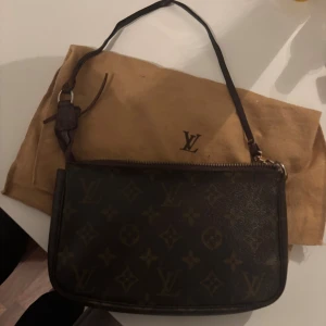 Louis Vuitton monogram axelväska - Säljer en klassisk Louis Vuitton axelväska i brunt skinn med ikoniskt monogrammönster och guldfärgade detaljer. Väskan har dragkedja upptill och en smal axelrem. Perfekt storlek för det viktigaste och levereras med original dustbag.