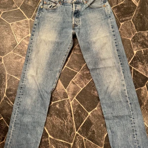 Levi's 501 ljusblå jeans straight fit - Klassiska Levi's 501 jeans i ljusblå tvätt med raka ben och fem fickor. Jeansen har knappgylf, ikonisk läderpatch bak och röd Levi's-tag vid bakfickan. Tillverkade i slitstark bomull med en straight passform som alltid är snygg.  Storlek w30 L 31