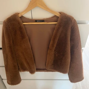 Brun pälsjacka från Gina Tricot - Säljer en brun pälsjacka från Gina Tricot med croppad passform och långärmade ärmar. Jackan har en mjuk och fluffig yta i syntetmaterial och är perfekt för att ge din outfit en trendig touch. Enkel att matcha med både jeans och klänning. Aldrig använd!