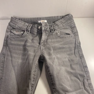 Grå jeans med broderad ficka Gina Tricot - Snygga grå jeans från Gina Tricot i storlek 170. Modellen har klassisk femficksdesign med extra detaljer som broderad bakficka och dekorativa knappar. Jeansen är flare och är tillverkade i mjukt denimtyg för en bekväm känsla.