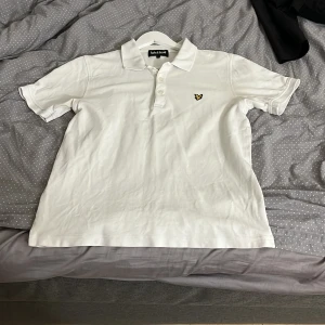 Vit pikétröja från Lyle & Scott - Vit pikétröja från Lyle & Scott i storlek L. Men passar även M. Klassisk krage, korta ärmar och tre knappar framtill. Tröjan har den ikoniska gula örnen broderad på bröstet. Tillverkad i mjuk bomull som är skön mot huden och passar perfekt till en chill stil. Tveka inte på att fråga eller skicka bud 