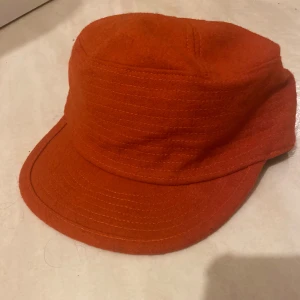 Mörkorange/ röd keps från Åhléns med prislapp - Snygg mörkorange/röd keps från Åhléns med klassisk form och böjd skärm. Kepsen är tillverkad i ett mjukt ull-liknande material och har svart innerfoder med resår för skön passform. Oanvänd o med prislapp kvar!
