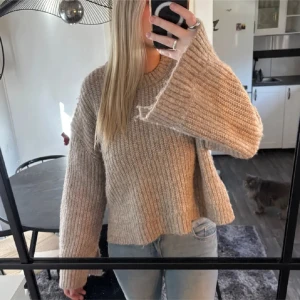 Beige stickad tröja med vida ärmar - Säljer en beige stickad tröja med ribbad struktur och vida, långa ärmar. Tröjan har en loose passform och rund halsringning. Supermysig och enkel att matcha med jeans eller leggings. Den har slits vid ärmen å midjan