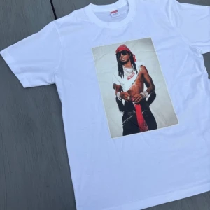 Supreme vit t-shirt med tryck - Supreme t-shirt i vitt med stort grafiskt tryck på framsidan på playboi carti. Klassisk rund hals och korta ärmar. Materialet är 100% bomull, vilket gör den skön och lätt att bära. Perfekt för dig som gillar streetwear och vill sticka ut.
