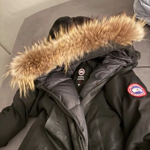  Canada Goose vinter jacka  - Säljer en svart dunjacka från Canada Goose med fluffig päls på huvan och klassisk röd logga på ärmen. Jackan har dragkedja, quiltad insida och justerbar huva. Perfekt för kalla vinterdagar och har en riktigt schysst oversized look.