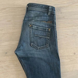 Diesel Darron jeans blå straight fit - Säljer ett par blå Diesel Darron jeans med straight fit och klassisk femficksdesign. Jeansen har slitningar och en reva på ena benet, men det ger en cool look (enligt mig) . Tillverkade i bomull med knappgylf och detaljerade sömmar. W30 och ca L32