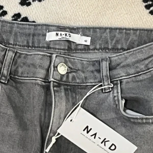 Grå bootcut jeans från NA-KD - Snygga grå jeans från NA-KD i bootcut-modell med klassisk femficksdesign och knappstängning. Jeansen har en rak passform över låren och lätt utsvängda ben, vilket ger en cool siluett. Materialet är robust denim och färgen är en neutral gråton.