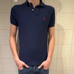 Marinblå pikétröja från Ralph Lauren - Snygg marinblå pikétröja från Ralph Lauren i fint skick! Jag på bilden är 184cm lång och väger 70kg. Hör av er vid frågor eller funderingar!👌✌️🤩