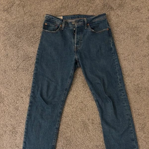 Levi's 501 blå jeans straight fit - Säljer ett par klassiska Levi's 501 jeans i blå denim med raka ben och knappgylf. Modellen är straight fit och har fem fickor, orange sömmar och Levi's Premium-märke bak. Perfekt för dig som gillar tidlös stil och äkta jeanskänsla. Storlek L 28 W 28. Hör av dig vid frågor osv! Paketet skickas inom 24h efter köp.