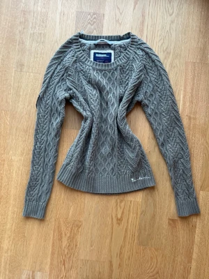 Bondelid kabelstickad tröja  - Kabelstickad tröja från bondelid i olivgrön/khaki färg. Den har en mer figursydd passform. Har även en detalj på ena ärmen som visas på bild 3. Köpt begagnad men i superfint skick.