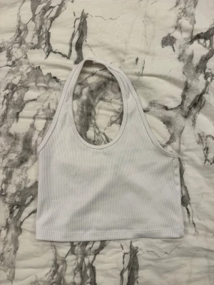 Vit ribbad linnetopp från H&M Divided - Säljer en enkel och snygg vit ribbad linnetopp från H&M Divided. Toppen har en croppad passform och är ärmlös med breda axelband och rundad halsringning. Perfekt att matcha med jeans eller kjol för en clean look.