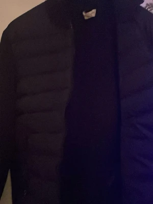 Svart cardigan från Moncler - Säljer en svart pufferjacka från Moncler i storlek M. Jackan har klassisk quiltad design, lång ärm och Moncler-logga på ärmen. Tillverkad i syntetmaterial och perfekt för kyliga dagar. Snygg och enkel att matcha till olika outfits.