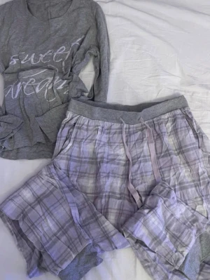 Grå pyjamas-set från Esmara - Mysigt pyjamas-set från Esmara i grått. Tröjan har trycket 'sweet dream' framtill och byxorna är rutiga med resår och dragsko i midjan. Mjukt material och ribbade muddar vid benslut. Perfekt för chillkvällar hemma.