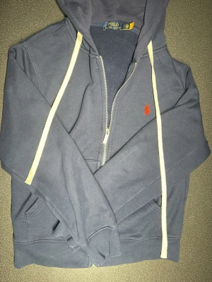 Blå hoodie från Polo Ralph Lauren - Polo Ralph Lauren hoodie, marinblå storlek S. Mycket bra skick knappt använd. Kan användas för både man och kvinna men är igentligen en manlig hoodie. Ny.