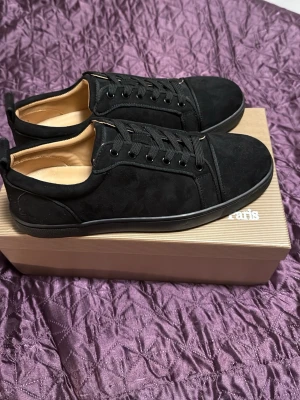 Christian Louboutin  - Stilrena svarta sneakers med låg profil och rund tå. Skorna har snörning och är tillverkade i mjuk mocka med diskreta sömdetaljer. Perfekta för dig som gillar en clean och klassisk look. Oandvända 