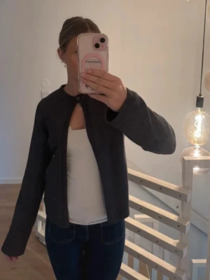 Mörkgrå kofta med knapp i halsen - En stilren mörkgrå kofta med rund halsringning och en knapp högst upp. Koftan har långa ärmar och är tillverkad i ett mjukt, stickat material. Från Gina tricot och använd väldigt få gånger🥰