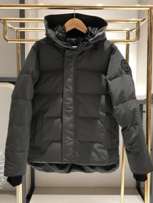 Svart dunjacka med huva - Snygg svart dunjacka från Canada Goose med huva och diskret logotyp på ärmen. Jackan har quiltad design, dragkedja framtill och lång ärm. Perfekt för kalla dagar och ger en clean, modern look.