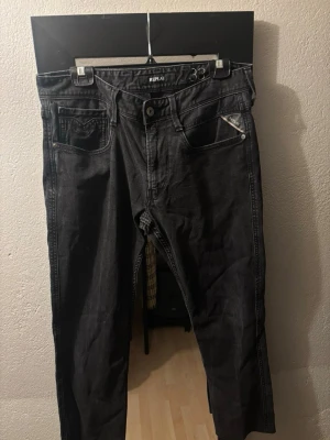 Svarta Replay jeans med raka ben - Säljer ett par svarta jeans från Replay med raka ben och klassisk femficksmodell. Jeansen har silverfärgade detaljer vid fickorna och en snygg tvättad look. Perfekta för dig som vill ha ett par stilrena och bekväma jeans.