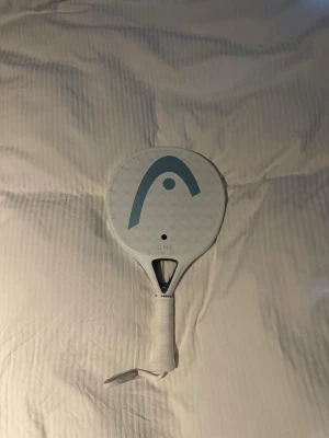 Head One Ultralight padelracket - Säljer ett vitt Head One Ultralight padelracket med stilren design och blå logga på träffytan. Racketen har rund form och greppvänligt handtag med vit linda. Perfekt för dig som vill ha ett lätt och smidigt racket till padelbanan. Detta är världens lättaste padelrack som bara väger 300 gram. Har bara blivit använd 2 gånger