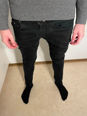 Svarta Morris jeans - Säljer ett par svarta Morris jeans med slim passform och klassisk femficksdesign. Jeansen har en snygg mörk ton och är tillverkade i mjukt jeansmaterial med stretch. Perfekt för dig som gillar stilrena och bekväma jeans.