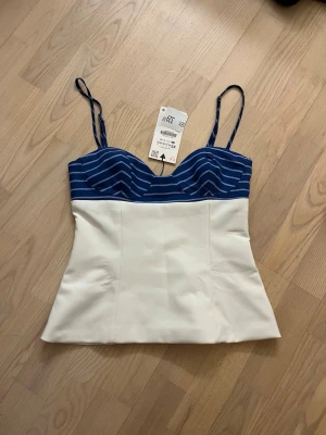 Vit och blå korsettopp  - Snygg korsettopp från Zara med smala axelband. Överdelen är blå med ränder och nedre delen är vit. Toppen har en figurnära passform och är perfekt för att lyfta vilken outfit som helst. Helt ny, aldrig använt💞
