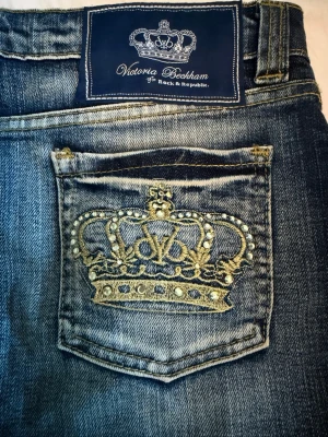 Victoria Beckham jeanskjol  - Säljer denna ursnygga jeanskjol från Victoria Beckham med cool tvätt! Kjolen har två bakfickor med ett komplett guldglittrande kronbroderi och pärldetaljer. Kjolen är som gott som ny💕Inga defekter finns! Hör av dig vid minsta fundering!💕✨