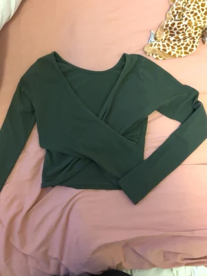 Grön omlottopp med lång ärm - Snygg grön omlottopp med långa ärmar, croppad passform och har en djup v-ringning.