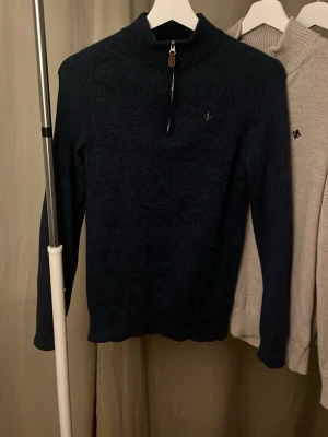 Mörkblå halvzip-tröja Morris - Mörkblå stickad tröja från Morris med halv dragkedja och liten broderad logga på bröstet. Tröjan har hög krage och ribbade muddar vid ärmslut och nederkant. Perfekt för lager på lager och stilren look storlek s men har krymt lite så är mer som xs/ xxs 
