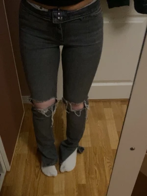 Grå slitna jeans med hål på knäna - Säljer ett par grå jeans med stora slitningar och hål över båda knäna. 