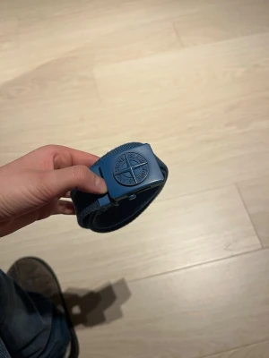Blå Stone Island bälte - Säljer ett blått bälte från Stone Island med klassiskt kompassmärke på metallspännet. De är mycket använt men funkar länge till säljer pga att de är för litet de är 85cm och är ett junior bälte nypris 1250kr hör av vid minsta lilla fråga 