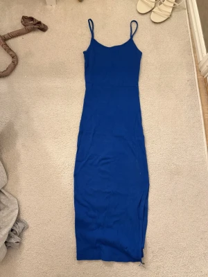Blå långklänning  - Säljer en ribbad blå långklänning från Amisu med smala axelband och slits på sidan. Klänningen är figurnära och har en enkel, stilren design som passar perfekt till sommaren. Materialet är mjukt och stretchigt för en bekväm känsla.