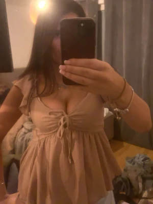 2 för 1 topp med snörning och volang - Supersöt beige topp med volangärmar och snörning framtill. Toppen har v-ringning och en luftig, flowy passform. Perfekt för dig som gillar en feminin och trendig stil.