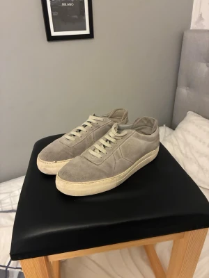 Arigato skor  - Snygga beige sneakers i mocka med klassisk låg profil och vita snören. Skorna har en rund tå och platt sula, vilket ger en clean och stilren look. Perfekta för dig som gillar minimalistisk stil och neutrala färger.