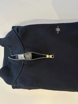 Marinblå halvzip från Gant - Helt ny Klassisk svart sweatshirt från Gant med halv dragkedja och liten broderad logga på bröstet. Tröjan har hög krage och är tillverkad i mjukt bomullsmaterial. Perfekt för en avslappnad och stilren look.