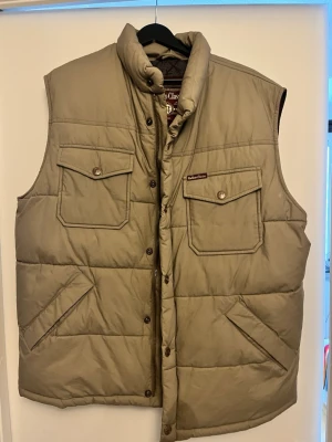 Beige dunväst från Marlboro Classics - Stilren dunväst från Marlboro Classics. Perfekt för lager-på-lager och outdoor-vibe. Bara fråga om ni undrar något.