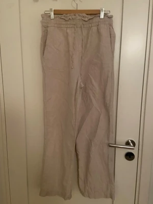 Beige linnebyxor från Cubus , storlek S - Säljer ett par ljusbeige linnebyxor från Cubus i storlek S. Byxorna har resår och snörning i midjan samt raka, vida ben. Perfekta för varma dagar och riktigt sköna att bära. Materialet är luftigt linne och modellen har en avslappnad passform.