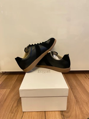 Maison Margiela  - Säljer ett par stilrena och tidlösa sneakers från Maison Margiela. Klassisk design i svart läder med kontrasterande gummisula, vilket ger en exklusiv och minimalistisk look som passar både vardag och mer uppklädda outfits.  ✨ Ikonisk Maison Margiela-design ✨ Högkvalitativa material och mycket bra komfort ✨ Levereras med original box   Färg: Svart Sula: Naturfärgad gummi Skick: Mycket bra  Hör av dig vid intresse. 