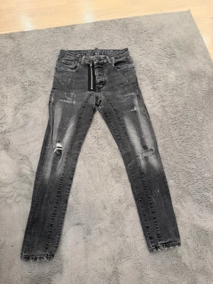 Grå jeans från dsquared  - Säljer ett par grå  jeans med slitningar och cool dragkedjedetalj framtill. Jeansen har en tvättad look, flera fickor och råa kanter vid bensluten. Perfekta för dig som gillar en edgy stil.