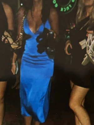 Blå långklänning i satin - Snygg blå långklänning i satinliknande material med smala axelband som korsas i ryggen. Klänningen har en omlott-v-ringad överdel och figurnära passform. Perfekt för dig som vill sticka ut med en elegant och trendig look.