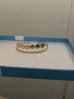 Guldfärgat armband med cirklar - Snyggt guld platerat armband med öppningsbar design. Armbandet har en rad med blanka, runda cirklar och en tunn rad med små gnistrande stenar undertill. Perfekt för dig som gillar trendiga och stilrena accessoarer.