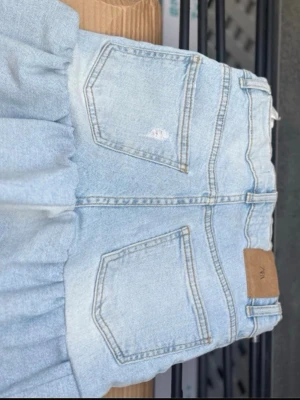 Ljusblå jeans från Zara, stl 152 - Säljer en ljusblå jeans kjol från Zara med volanger. Jeansen har en snygg tvätt och patch med Zara-logga bak i midjan. Perfekta för en chill och trendig look.