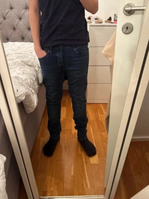 Mörkblå slim straight jeans från jack&jones  - Säljer ett par mörkblå Levi's jeans i klassisk straight modell med slim passform. Jeansen har fem fickor, normal midja och subtila slitningar framtill för en snygg vardagslook. Tillverkade i mjuk bomullsdenim med lite stretch för extra komfort.