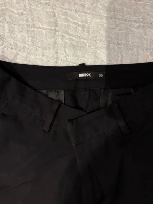 Svarta kostymbyxor från BikBok - Klassiska svarta kostymbyxor från BikBok med raka ben och hällor för bälte. Byxorna har en stilren look och är tillverkade i ett mjukt material som känns bekvämt hela dagen. 