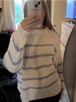 Vit stickad tröja med  blå ränder - Mysig stickad tröja i vitt med horisontella blå ränder. Tröjan har rund halsringning, avslappnad passform och långa ärmar. Perfekt för lager på lager och chill dagar. Sitter som S