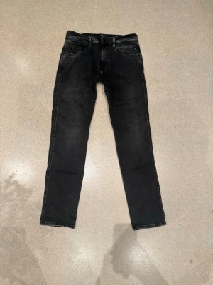 Svarta Replay Anbass jeans herr - Snygga svarta Replay Anbass jeans med klassisk femficksdesign och diskreta slitningar. Jeansen har en smal passform och är tillverkade i mjukt bomullsmaterial med stretch för extra komfort. Perfekta för en trendig och avslappnad look.