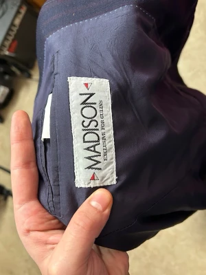 Mörkblå randig kavaj från Madison - Snygg mörkblå kavaj från Madison med diskreta ränder och två knappar framtill. Klassisk passform med långa ärmar och två fickor. Perfekt för dig som vill ha en stilren och tidlös look.