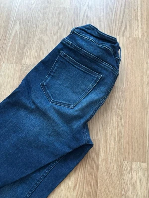 Mörkblå bootcut jeans med fickor - Säljer ett par mörkblå jeans med bootcut passform och markerade sömmar längs benen. Jeansen har  framfickor och klassisk femficksdesign. Materialet är stretchigt jeans och färgen har en snygg tvättad look.