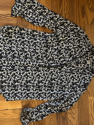 Svartvit mönstrad blus från H&M - Snygg svartvit blus från H&M med abstrakt mönster. Blusen har lång ärm och knäppning framtill. Tillverkad i ett lätt och luftigt material som känns skönt mot huden. Perfekt för dig som gillar trendiga mönster och vill sticka ut lite extra.
