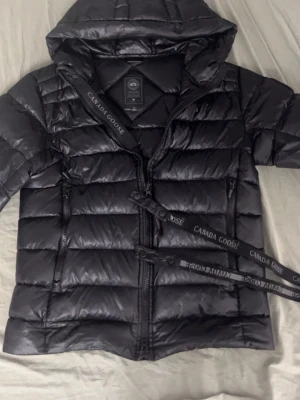 Canada Goose Crofton - Snygg svart dunjacka från Canada Goose med huva och tvåvägsdragkedja. Jackan har quiltad design, Det finns också lite repa som jag har täckt med svart tejp och finns små hål nära fickan som inte syns mycket!